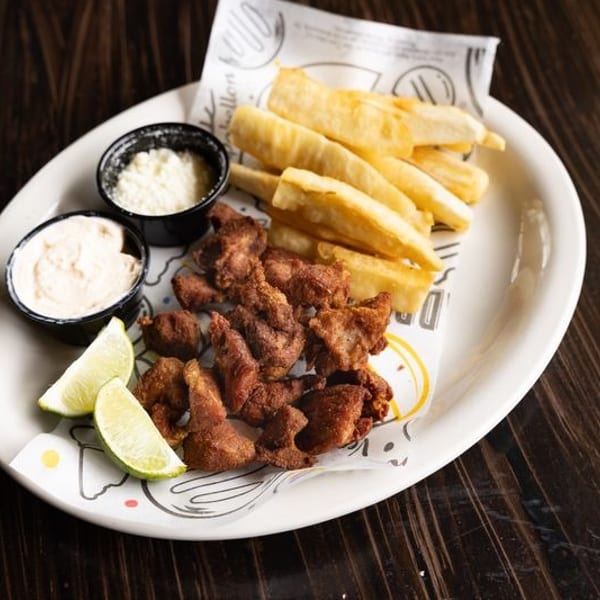Plate of crispy fried meat, golden fries, dipping sauces, and lime wedges on a restaurant table.