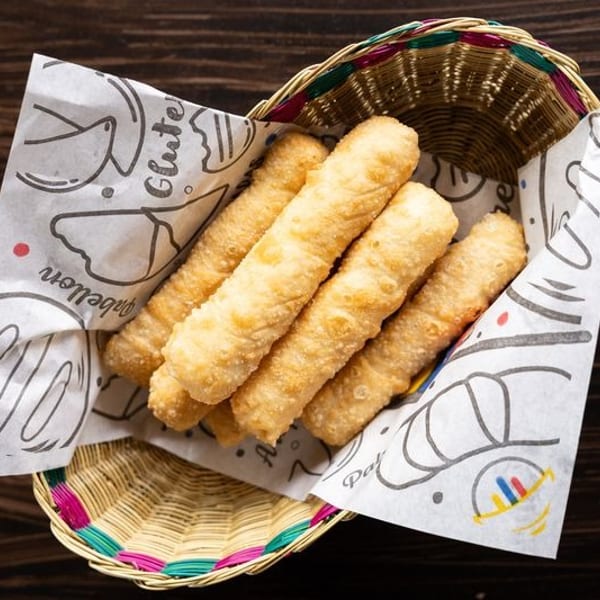 Basket of golden fried dough sticks lined with illustrated paper on a dark wooden table.